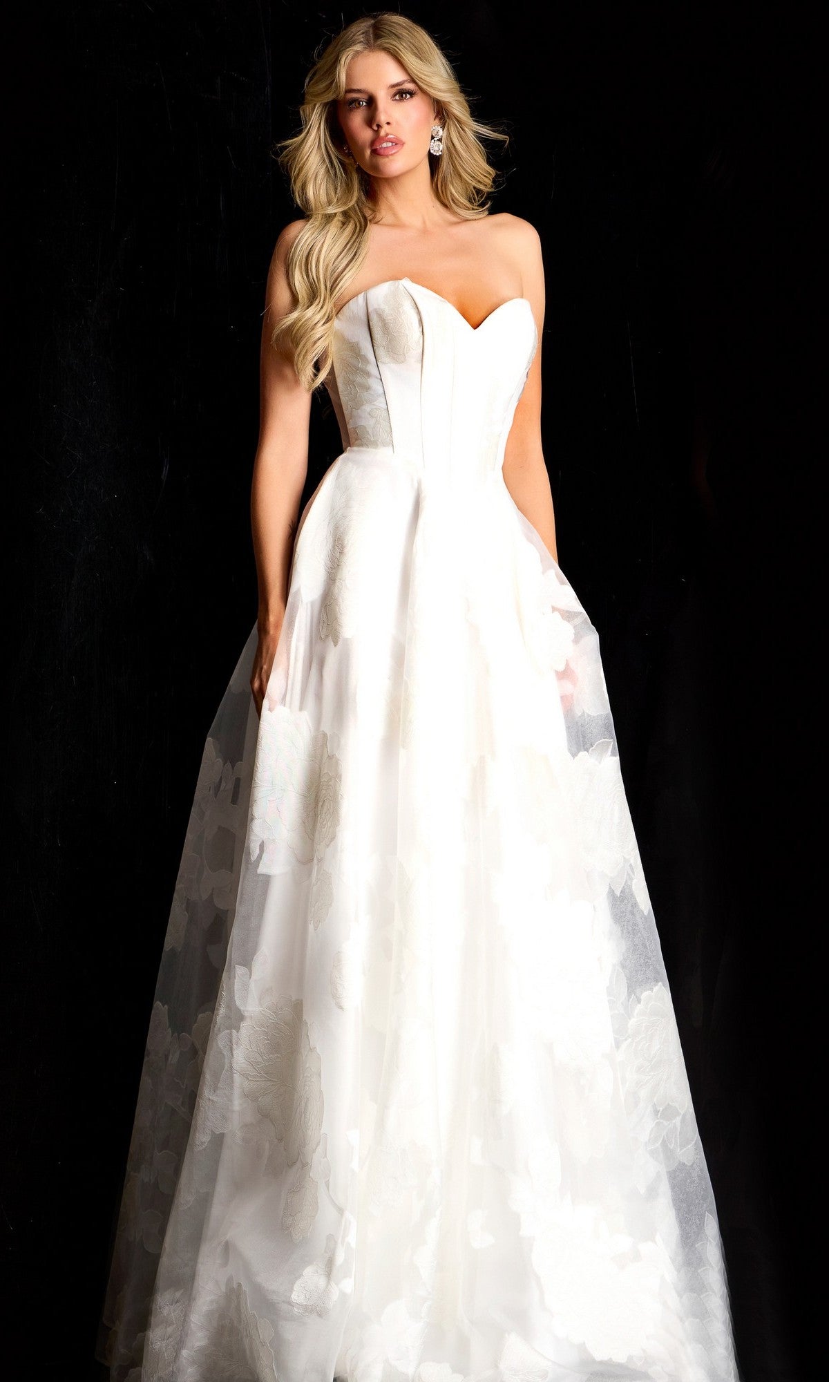 A woman stands against a black background wearing the Long Prom Dress: Jovani 47327, featuring a strapless white corset bodice and a full, floor-length skirt.